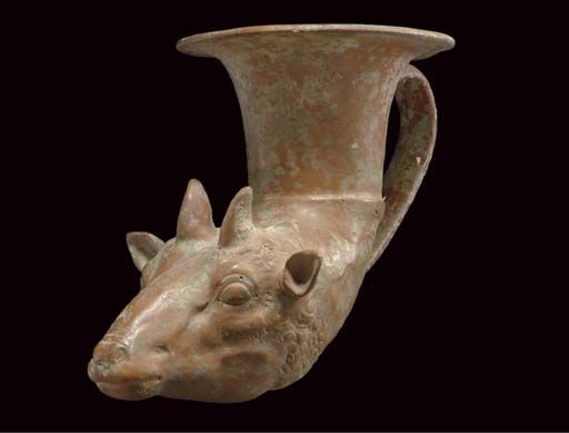 A GREEK POTTERY RHYTON CLASSICAL PERIOD, CIRCA MID 4TH CENTURY B.C. Probably from Tarentum, of unglazed buff-colored fabric, molded in the form of a sheep's head, with projecting triangular ears, short splayed horns, and lidded convex almond-shaped eyes, the bowl with a flaring rim and a strap handle 9½ in. (24.1 cm.) long