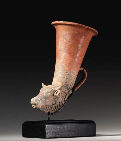 A WESTERN ASIATIC POTTERY RHYTON circa 5th-4th century b.c. Perhaps Achaemenid, with a bull's head protome, the wide almond-shaped eyes with articulated pupils and irises below ridged and incised brows, the nose stippled, the pattern of the grooved ridges of the dewlap accented by the horizontal bands painted on the conical bowl, with a single handle in back and a flaring lip, the spout a protruding through the chin 9 in. (22.8 cm.) long