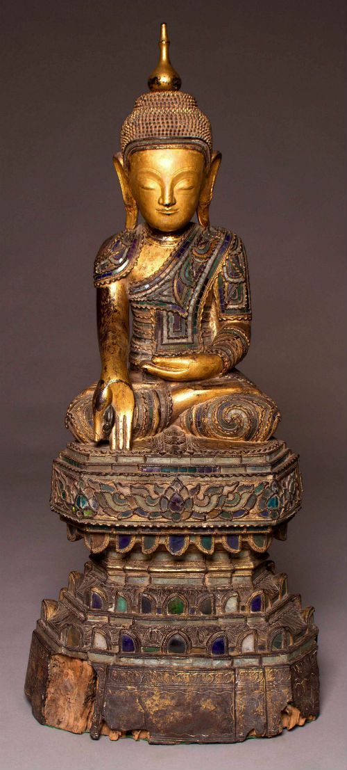 Large 18thC Burmese Shan Buddha sculpture carved from Teak lacqured and inlayed with glass fragments and gilded with gold leaf. Seated on a high altar this buddha has a very fine look and perfect poise. We purchased this sculpture last year from a collector in Kensington London along with the [13th-14thC Thai Fragmentary Ayutthaya Period Buddha]. Since then we have been doing research on the feint inscription on the lower part of the altar. Which has been translated by the Wat Sai Moon monastery