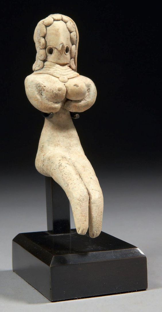 STATUETTE DE FEMME ASSISE. Figurine de femme en position assise, les jambes tendues, les bras placÃ©s sous une gÃ©nÃ©reuse poitrine. La tÃªte stylisÃ©e prÃ©sente une coiffure formÃ©e de boucles frontales et temporales et elle porte un large collier de quatre bourrelets. Terre cuite. VallÃ©e de l'Indus, culture de Mehrgarh, ca. 2800-2600 av. J.-C.